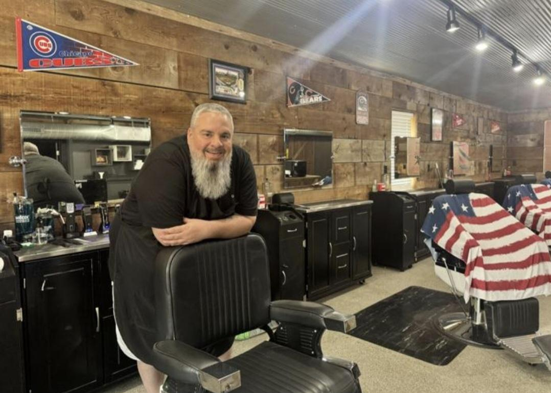 Josh Powell standing behind a barber chair in his Silvis shop